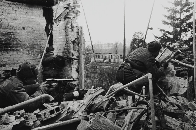 Three soldiers firing from behind a broken building