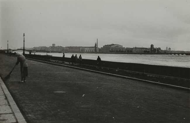 View of woman in scarf sweeping street adjacent to river, Leningrad
