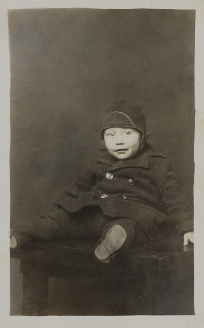 Carldowen Handcock in Winter Cap and Coat (seated on a table)