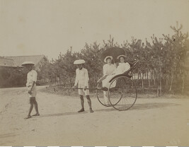 Man standing next to a woman in a rickshaw pulled by two Japanese men. Kamakura, Kanagawa Prefecture,...