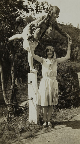 Woman Balancing on Post with Leg Raised; another Woman Supporting Her