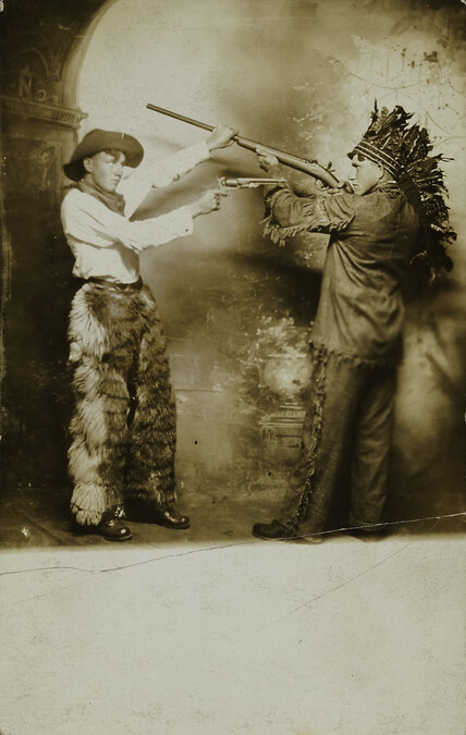 Two Young Men, dressed as a Cowboy and Native American, Pose Fighting Each Other with a Gun and Rifle, respectively