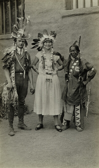 Couple dressed in Native American Regalia standing next to Native American man