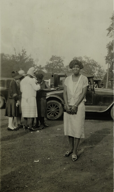 Woman in Hat Posing with Car and Group of Three Women and a Man in Background